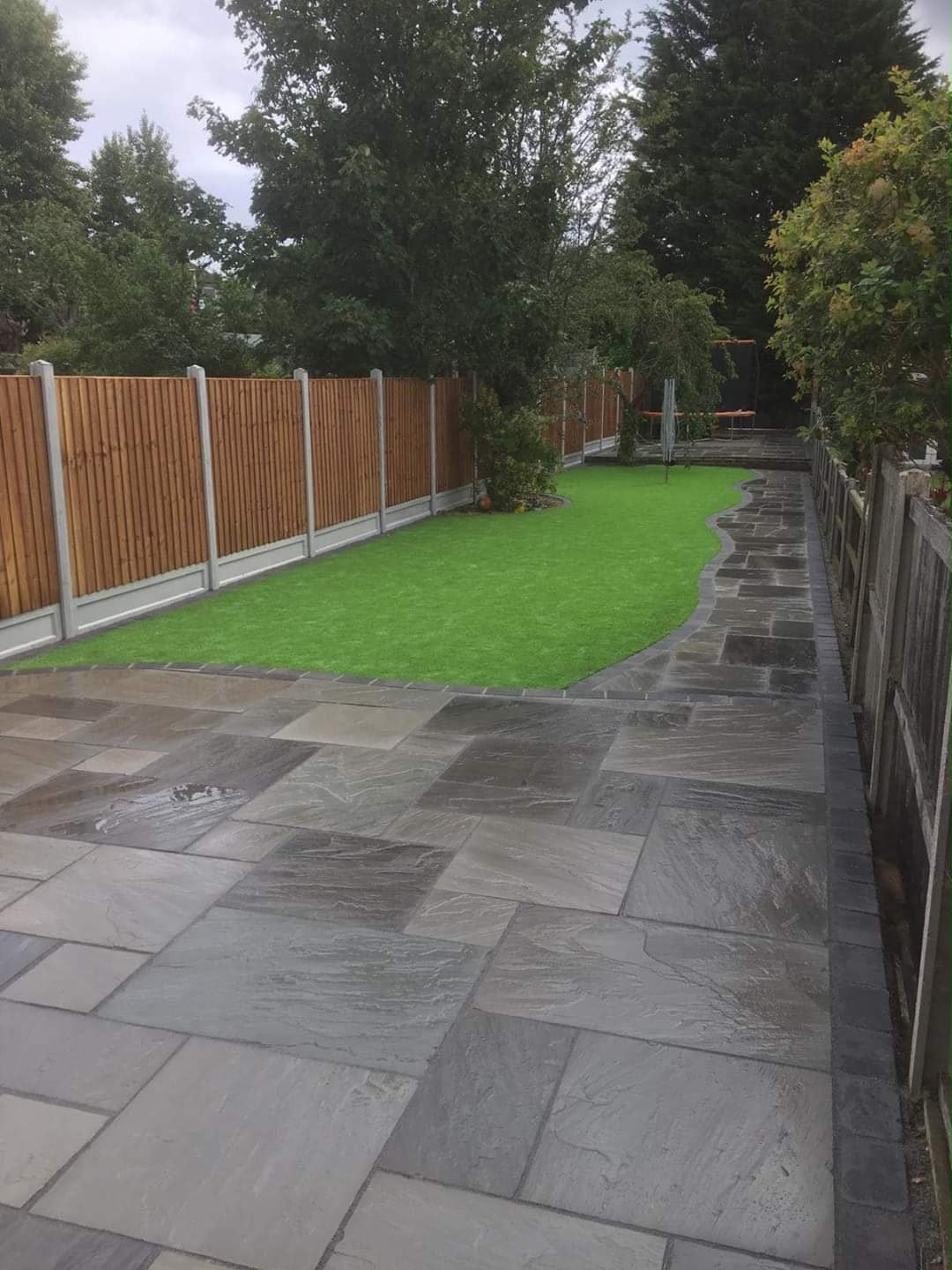 Dark stone patio meeting artificial grass at the rear of a house